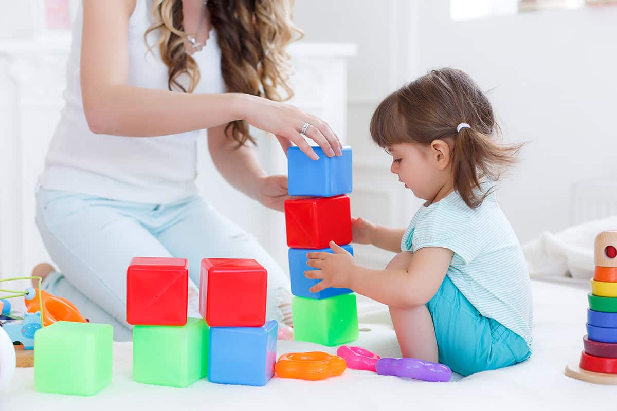 image of a woman helping a young girl stack blocks