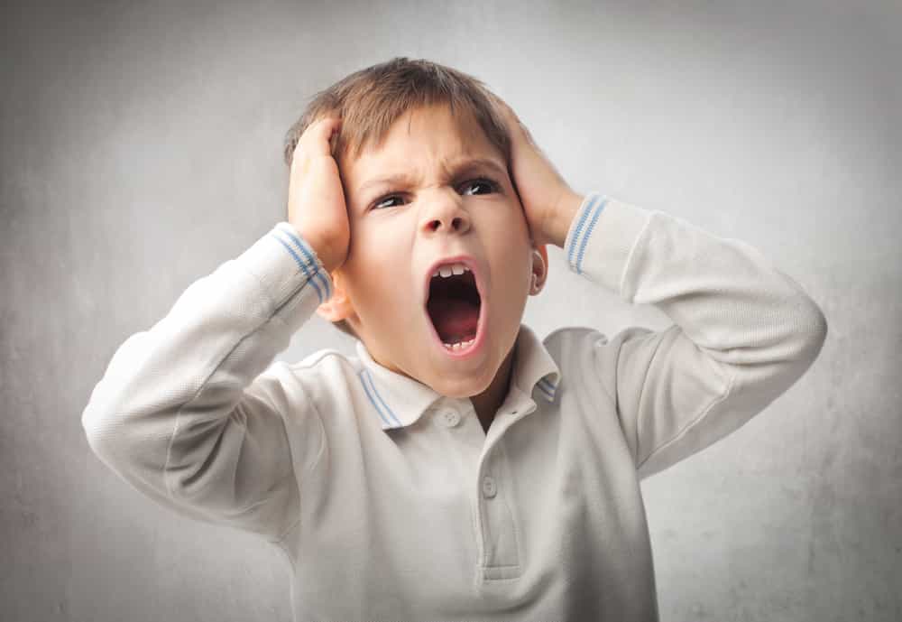 a young boy holding his head while yelling.